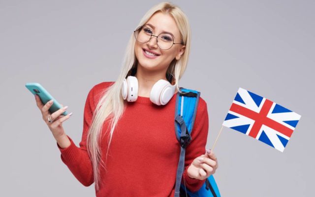 online-education-foreign-language-translator-english-student-smiling-blond-woman-headphones-holding-mobile-phone-british-flag-grey-space-distance-learning (1)